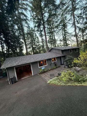 Gray-sided home among tall firs with its new shingle roof