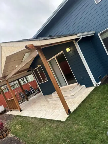 New covered patio with tile floor beside a blue house